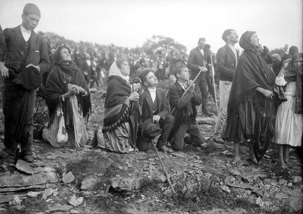 A black-and-white photo showing many people congregated on a rocky hillside, in suits and shawls and dresses, mostly staring up at the sky.